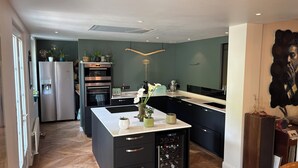 Een moderne keuken met een centraal eiland, inbouwovens en een wijnkoeler.