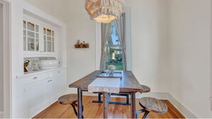 A dining area with a wooden table, chairs, a chandelier, and a view through a window. - “Henry’s Haus” | Walk to Main | Pet Friendly! (Fredericksburg)