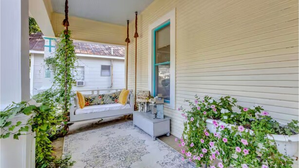 A covered porch with a white bench, a small table, and potted plants. - “Henry’s Haus” | Walk to Main | Pet Friendly! (Fredericksburg)