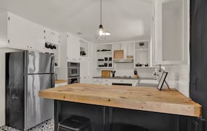 A modern kitchen with white cabinets, stainless steel appliances, and a wooden island. - NEW "House In Black" | Pool | Hot Tub | Bohemian (Fredericksburg)