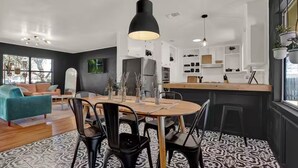 Een moderne keuken met een centraal eiland, een eethoek met een ronde tafel, en een woonkamer met een blauwgroene bank.