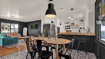 A modern kitchen with a central island, a dining area with a round table, and a living room with a teal sofa.