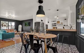 A modern kitchen with a central island, a dining area with a round table, and a living room with a teal sofa. - NEW "House In Black" | Pool | Hot Tub | Bohemian (Fredericksburg)
