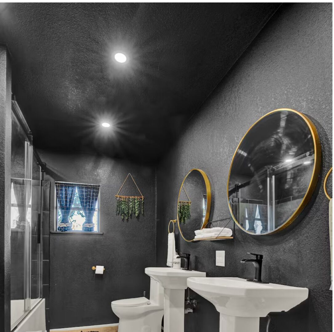 Un bagno con due lavandini, un WC, una doccia e una finestra con tende.