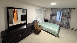 Quarto com cama, cômoda, cadeira, espelho, janela com cortinas e aparelho de ar condicionado.