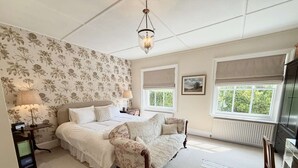 A bedroom with a bed, a chair, a nightstand, a lamp, a picture on the wall, and a window with a view of greenery. - St Davids by NewFo dot Rest (Milford on Sea)