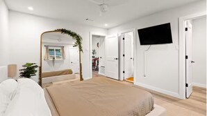 Un dormitorio con una cama, televisión, ventilador de techo y una puerta que da a otra habitación.