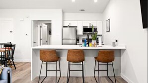 Una cocina moderna con gabinetes blancos, un refrigerador de acero inoxidable y una barra con dos taburetes.