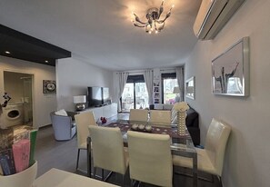 Ein modernes Wohnzimmer mit Essbereich, einer Kronleuchter und einem Fernseher.