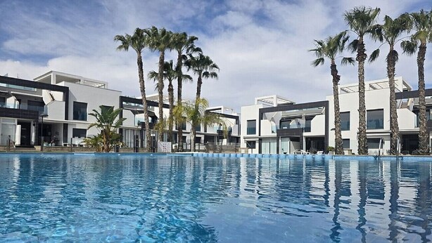 A swimming pool with modern buildings and palm trees in the background. - Groundfloor, oasis beach VI la zenia (La Zenia)
