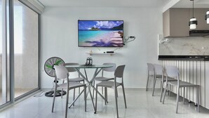 A modern dining area with a glass table, metal chairs, a wall-mounted TV, and a fan. - Cozy apartment, location to enjoy the beautiful Cartagena/Colombia. (Cartagena de Indias)
