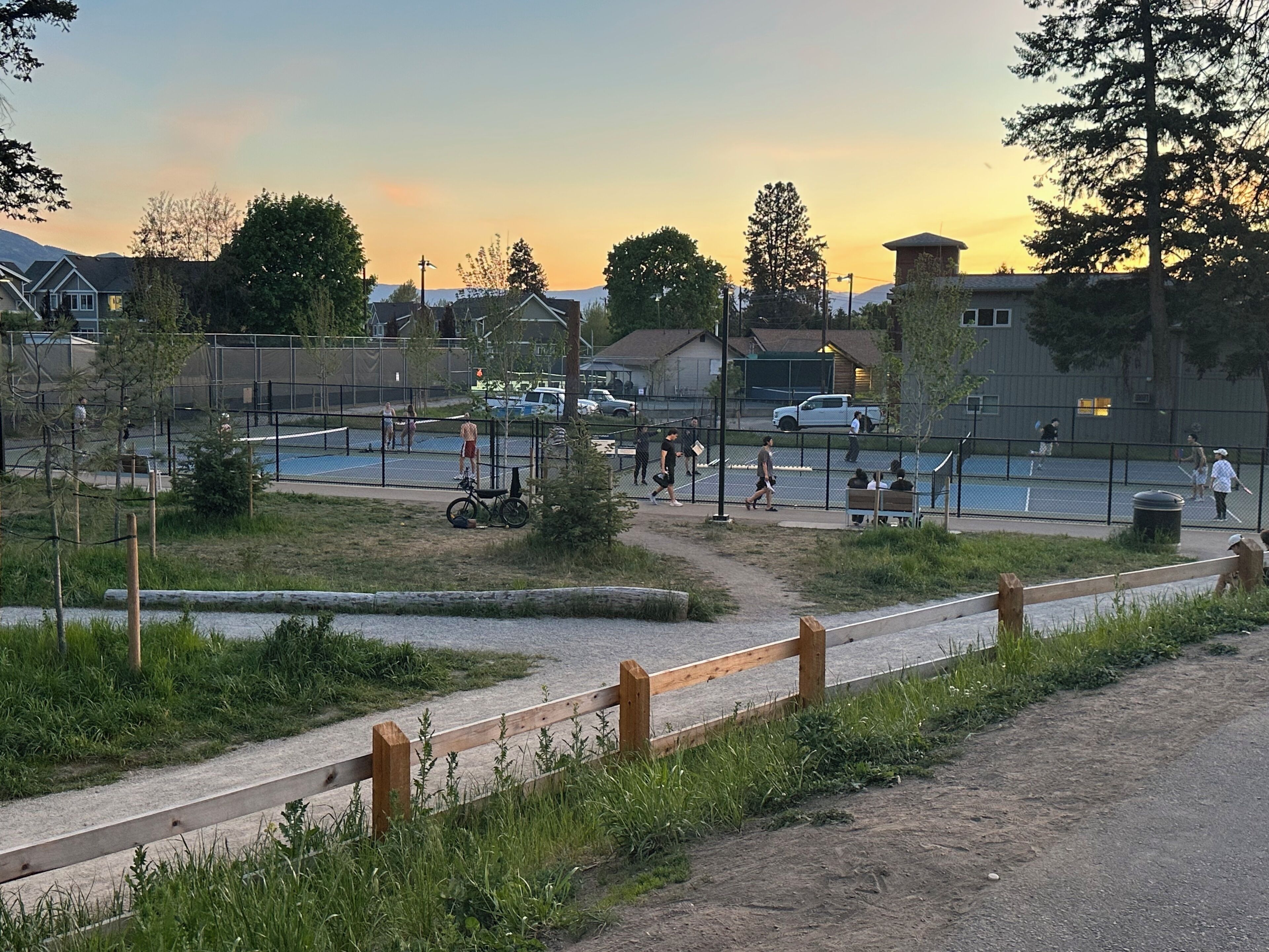 Un espace extérieur clos, comprenant un court de tennis, une clôture en bois et un chemin de terre.
