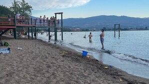 A beach with a wooden pier, people swimming, and a mountain in the background. - Upper Mission Casita | Boutique Lakeview Suite for Business or Leisure (Kelowna)