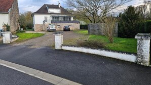 Een oprit met een huis, geparkeerde auto's en een toegangshek.