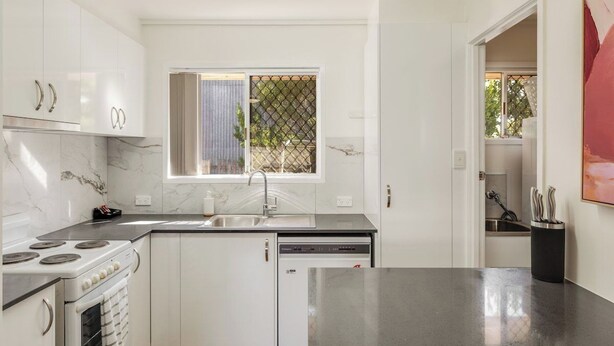Una cucina moderna con mobili bianchi, un piano di lavoro nero, una finestra vista e una lavastoviglie.