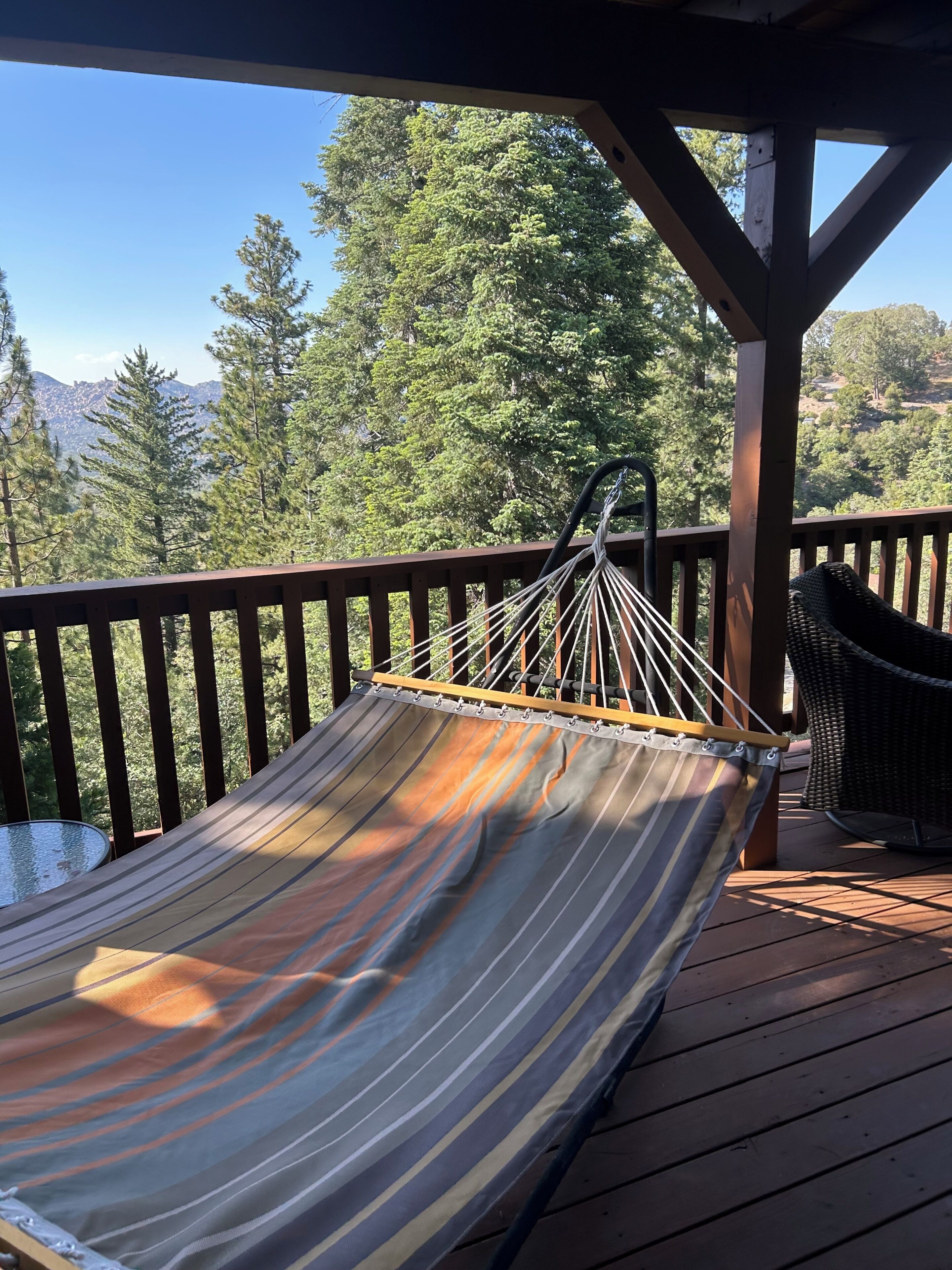 A hammock on a wooden deck with a view of trees and mountains.