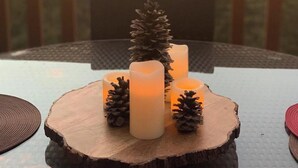Una mesa con velas y piñas sobre una tabla de madera, ubicada en un balcón con vistas a montañas y luces colgantes.