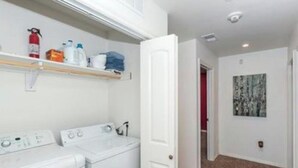 Una sala de lavandería con ropa apilada, un extintor y una puerta que da a otra habitación.