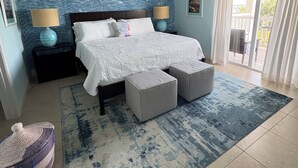 A bedroom with a bed, two bedside tables, a ceiling fan, a large window with curtains, and a patterned wall. - Fully Furnished 2BR/2BA Bimini Bay Condo (Bimini)