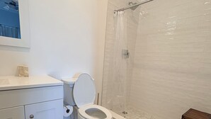 A bathroom with a toilet, a shower, and a small wooden stool. - Fully Furnished 2BR/2BA Bimini Bay Condo (Bimini)