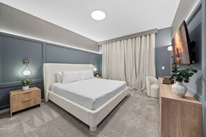 A modern bedroom with a large bed, bedside tables, a TV, and a desk with a plant. - 7BR house with game room near Disney area (Kissimmee)