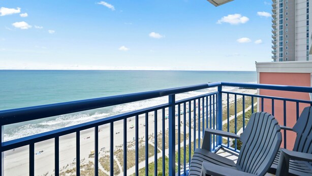 A balcony with a view of the beach and ocean, two Adirondack chairs, and a tall building in the background. - TOP Floor 2bd/2ba Oceanfront Master w Free Wi-fi (Myrtle Beach)