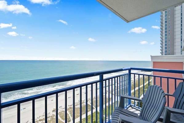 A balcony with a view of the beach and ocean, two Adirondack chairs, and a tall building in the background. - TOP Floor 2bd/2ba Oceanfront Master w Free Wi-fi (Myrtle Beach)