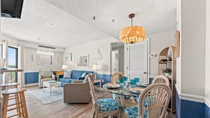 A modern living room with a dining area, featuring a chandelier, wicker furniture, and a view of the outdoors. - MB RESORT (Myrtle Beach)