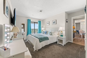 A bedroom with a bed, bedside tables, a dresser, a mirror, and a window with curtains. - MB RESORT (Myrtle Beach)