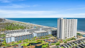 A high-rise hotel with multiple floors, a parking lot, and a view of the beach. - MB RESORT (Myrtle Beach)