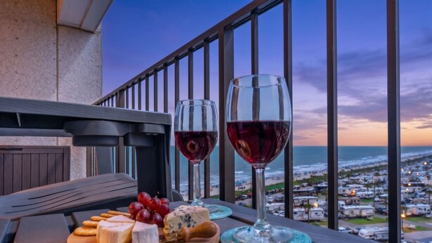 A balcony with a table set for a meal, featuring cheese, grapes, and wine glasses. - MB RESORT (Myrtle Beach)