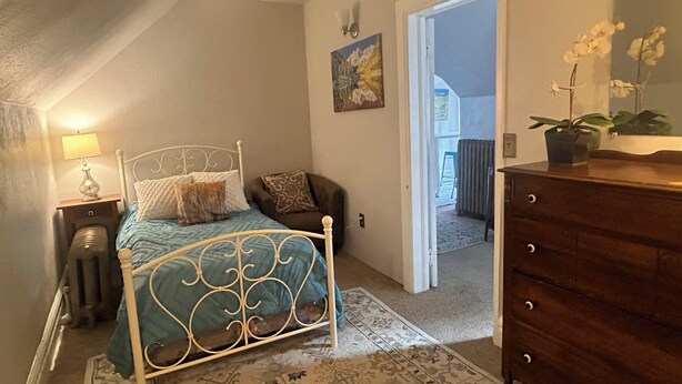 A bedroom with a metal bed frame, a bedside table with a lamp, a dresser, and a door leading to a balcony. - The Garden House on Emerson - Capitol Hill 2/1 walkable to down + parking + deck (Denver)
