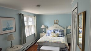 Una camera da letto con un letto, comodini, una lampada da comodino, una finestra con tende, un quadro appeso al muro e un tavolino con una lampada.