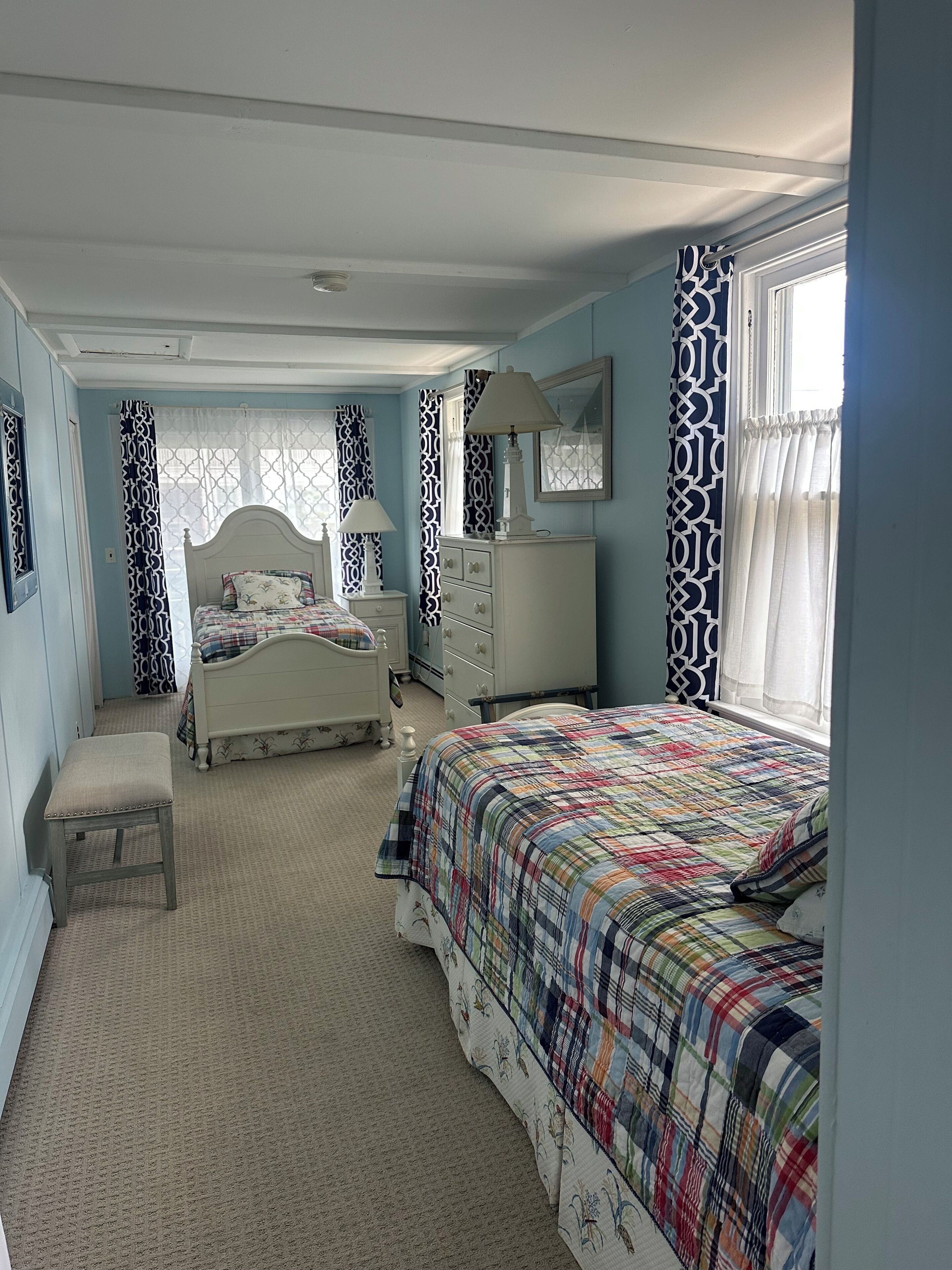 A bedroom with a bed, a nightstand, a dresser, a bench, and a window with patterned curtains.