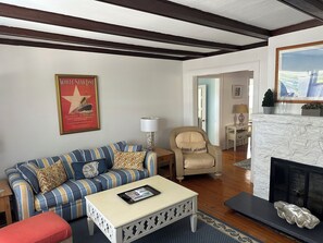 Ein Wohnzimmer mit einem gestreiften Sofa, einem kleinen Tisch mit einem Tablet, einem Sessel mit Kissen, einem Kamin und einem Poster an der Wand.