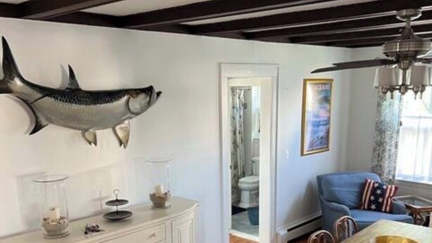 Zona pranzo con tavolo e sedie in legno, una cassettiera bianca, un quadro raffigurante pesci e una ventola a soffitto.