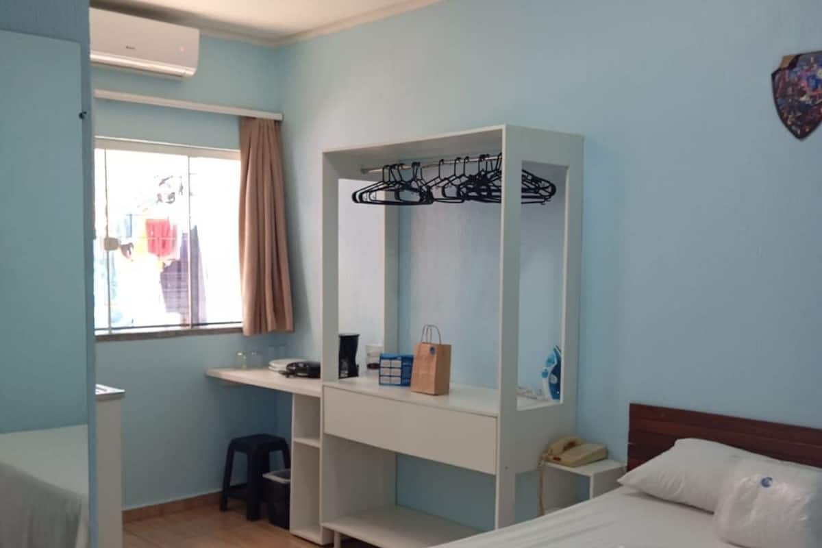 Una habitación de hotel con cama, escritorio y silla, armario y ventana con cortinas.