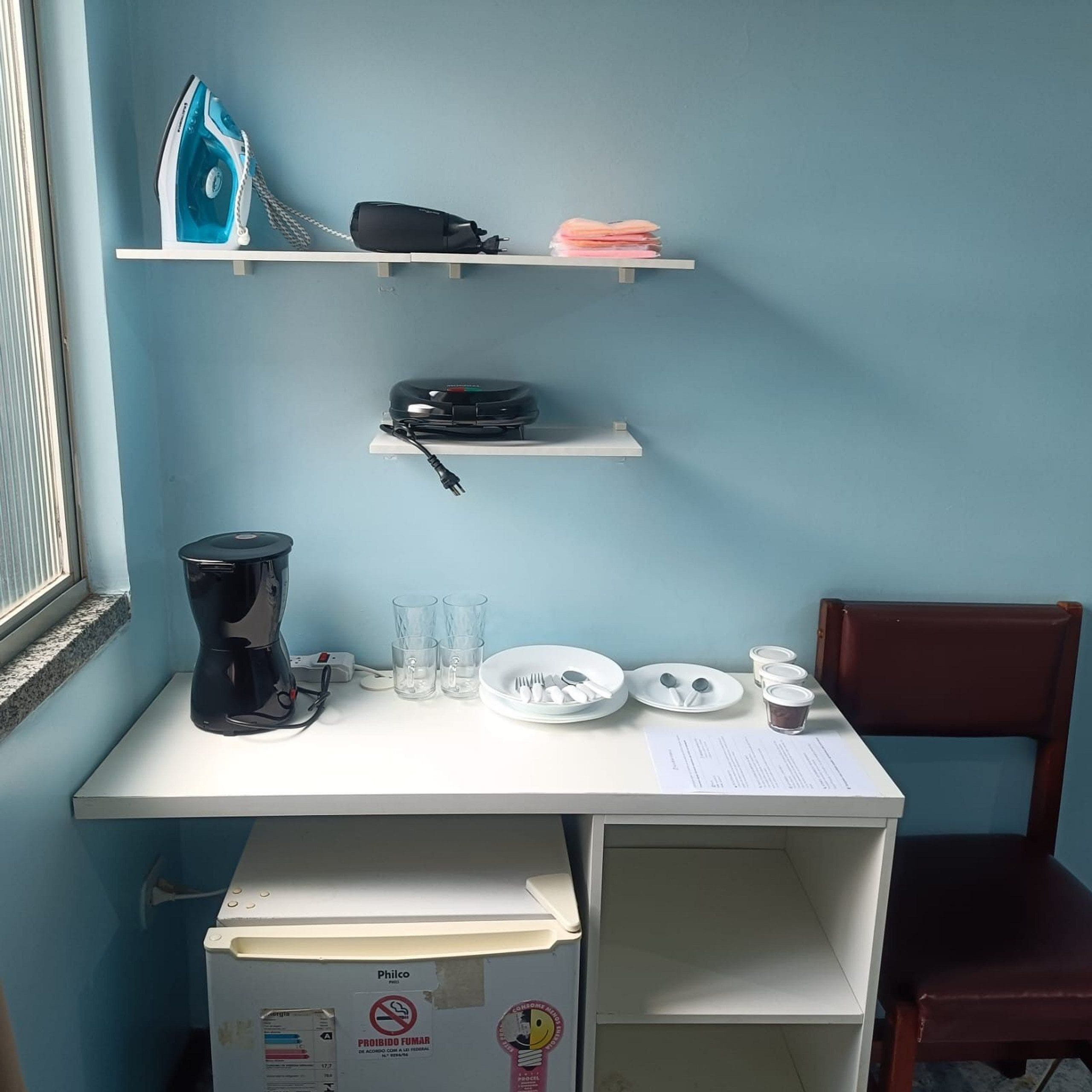 A small workspace with a desk, a coffee maker, a plate with utensils, and a chair.