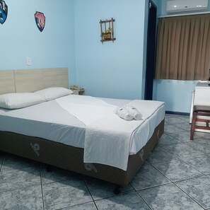 Uma cama com lençóis brancos, cabeceira de madeira e uma pequena mesa de cabeceira com abajur.