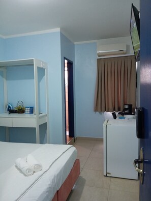 A hotel room with a bed, a desk with a chair, a television, and a refrigerator.