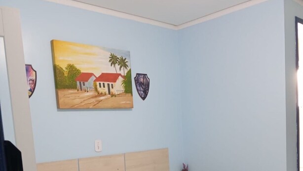 A bedroom with a bed, a nightstand, a painting, and a shield-shaped decoration on the wall. - Residencial Wolverine  (Foz do Iguaçu)