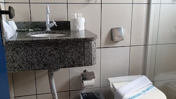 Un baño con lavamanos de granito, inodoro, cubo de basura y perchero para toallas.