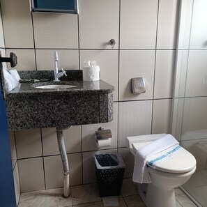 A bathroom with a granite sink, a toilet, a trash bin, and a towel rack.