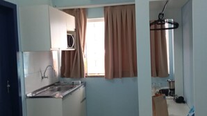 A compact kitchen with a built-in stove, a sink, and a window with curtains. - Residencial Wolverine  (Foz do Iguaçu)