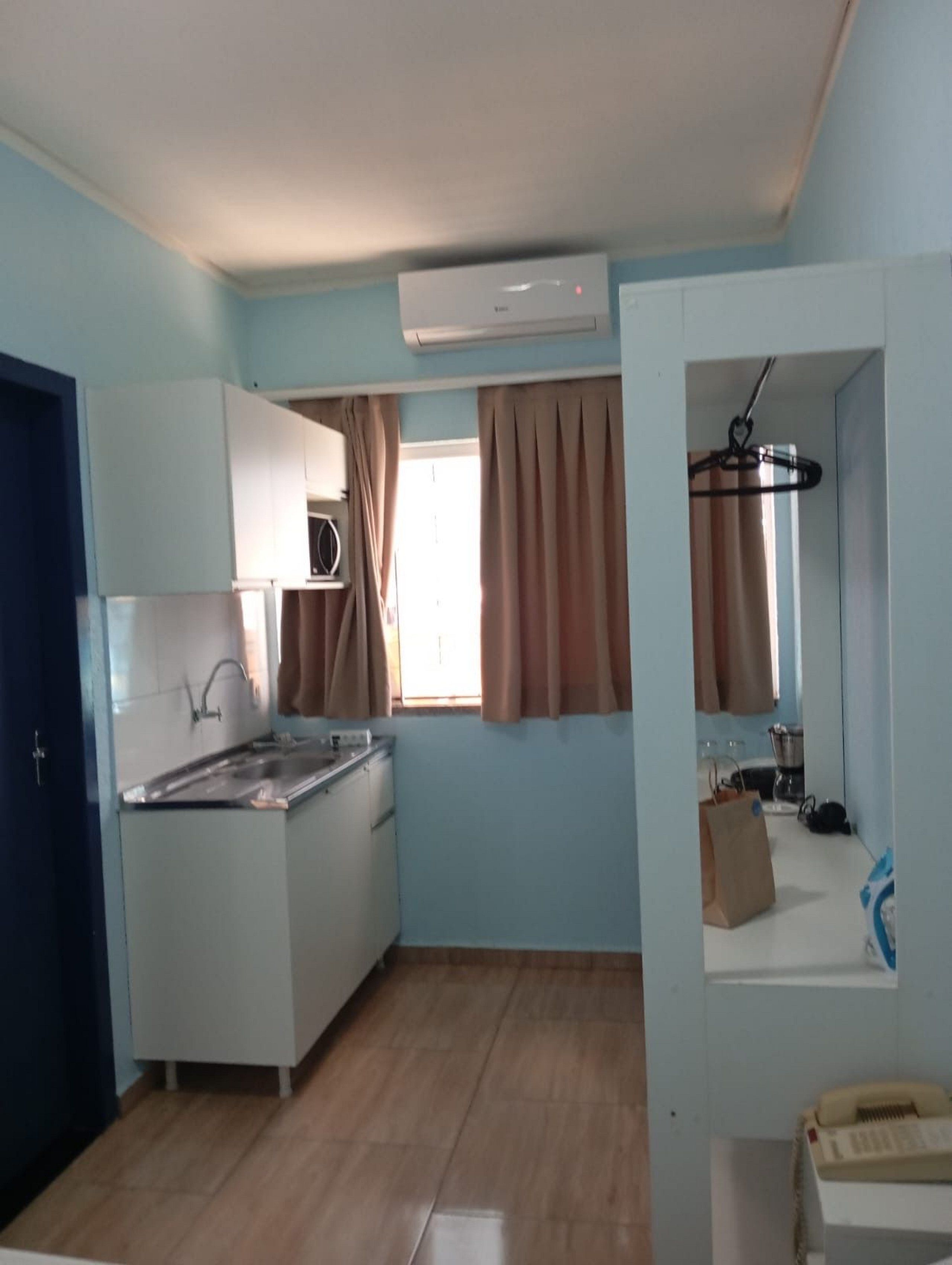 Una cocina compacta con estufa integrada, un lavamanos y un ventanal con cortinas.