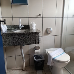 A bathroom with a granite sink, a toilet, a trash bin, and a towel rack.