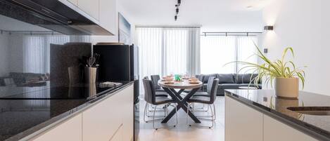 A modern kitchen with a dining area, a sofa, and a potted plant.