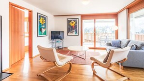 Una sala de estar moderna con un sofá, dos mecedoras, un televisor y un balcón con vistas.