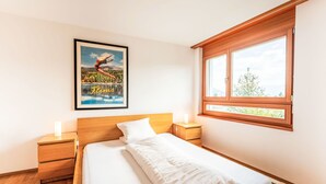 Un dormitorio con una cama de madera, una mesita de noche con lámpara, una ventana con vistas y un cuadro en la pared.