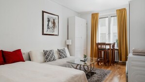 Ein modernes Hotelzimmer mit einem Bett, einem kleinen Tisch, einem Sessel, einer Couch, einem Gemälde und Blick ins Freie.